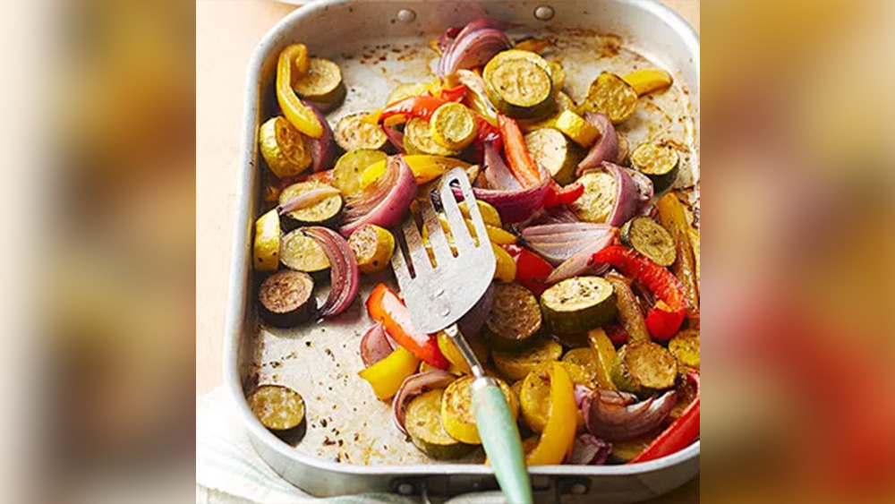Oven roasted zucchini red onion yellow squash and herbs in silver sheet pan
