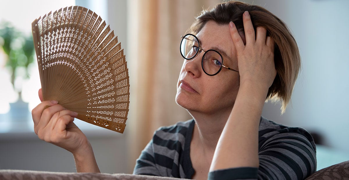 Exhausted middle aged woman waving her fan, suffering from menopausal symptoms, experiencing hot flush