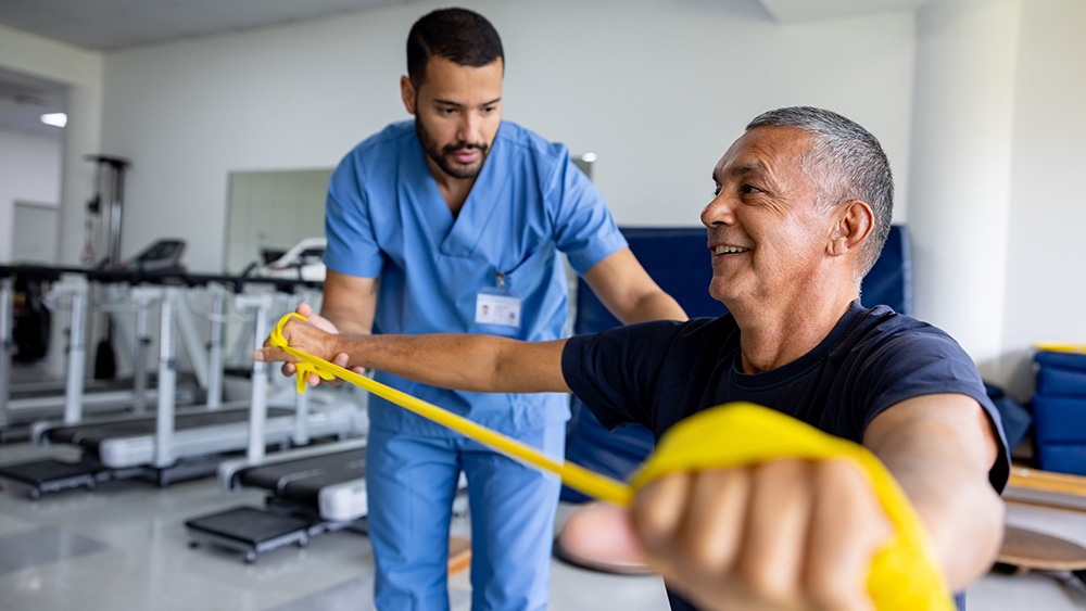 Young Black male physical therapist helping smiling older Black male patient using resistance band
