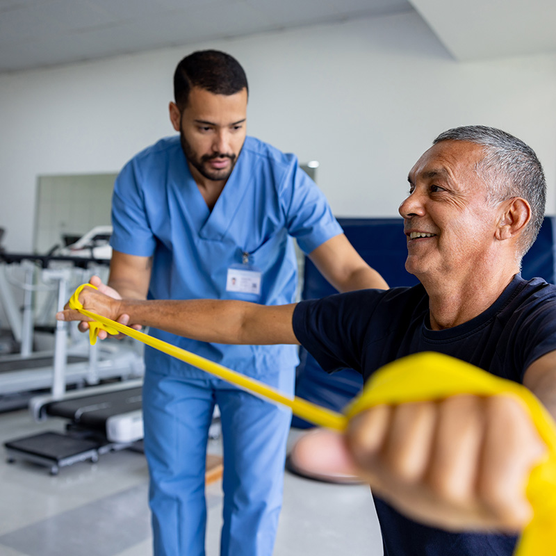 Young Black male physical therapist helping smiling older Black male patient using resistance band