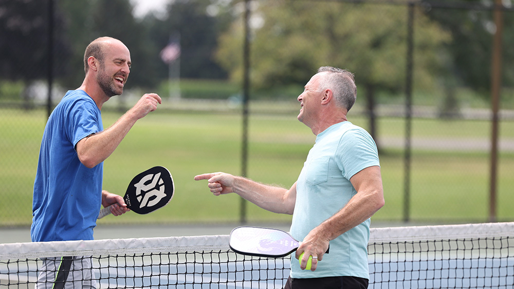 Two handsome white men point and smile at each other after a pickleball match