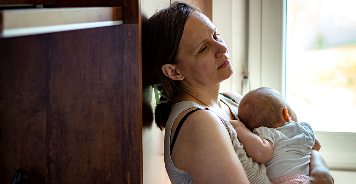 Tired concerned mother rocking sleeping baby in kitchen