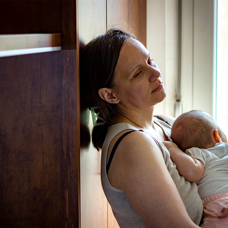 Tired concerned mother rocking sleeping baby in kitchen