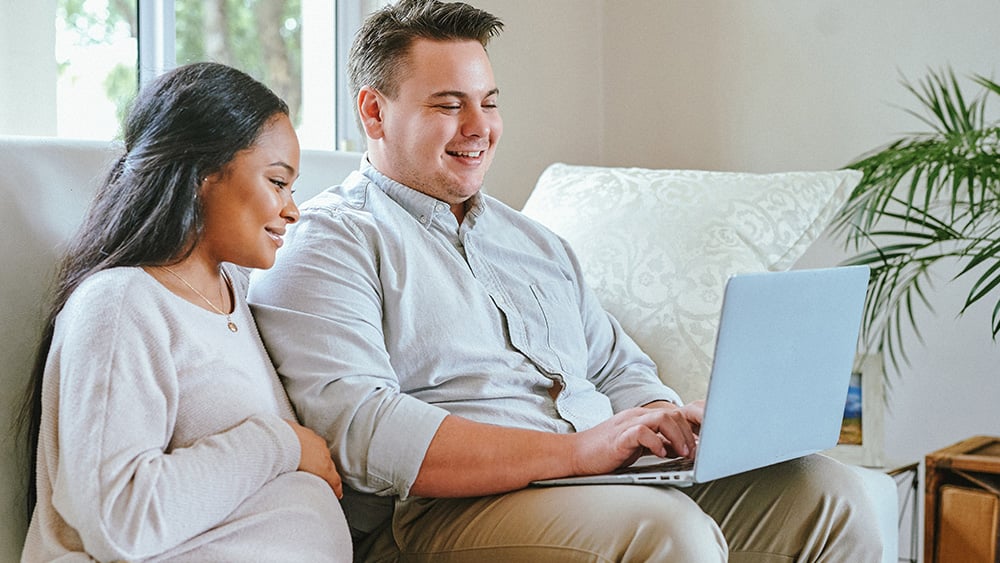 Shot of a man working on his laptop while sitting at home with his pregnant wife