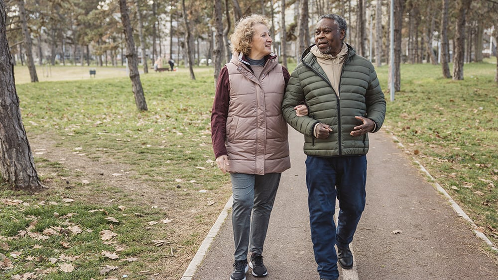 Middle aged white woman and Black man walk outdoors on path in woods in cooler weather