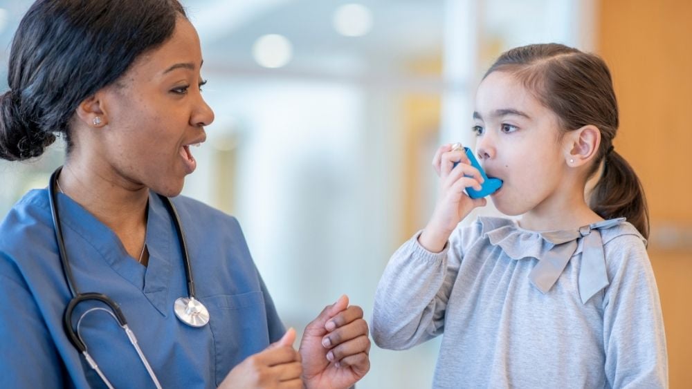 Doctor with young female child using inhaler for asthma