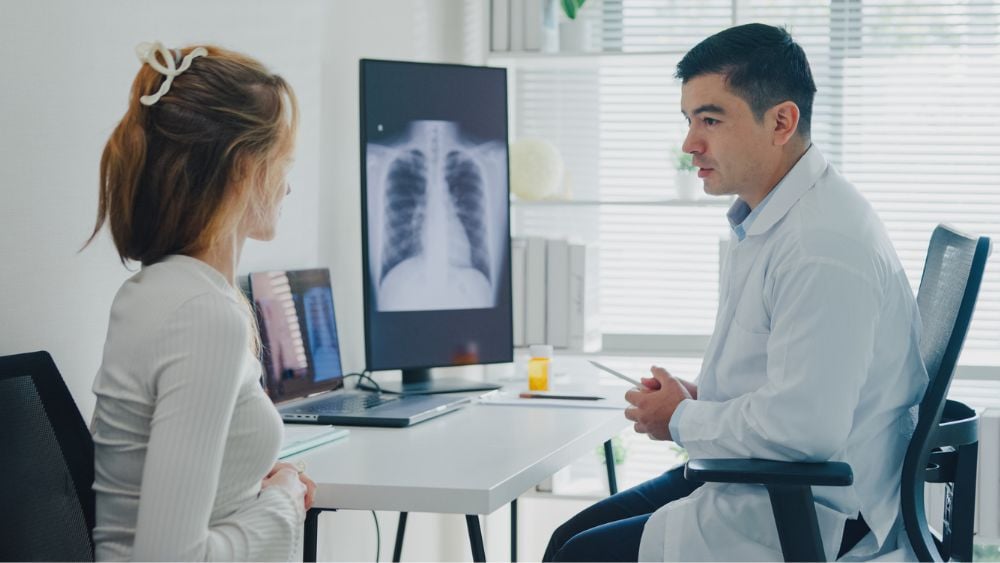 Female patient discussing lung condition with male doctor xray image on screen