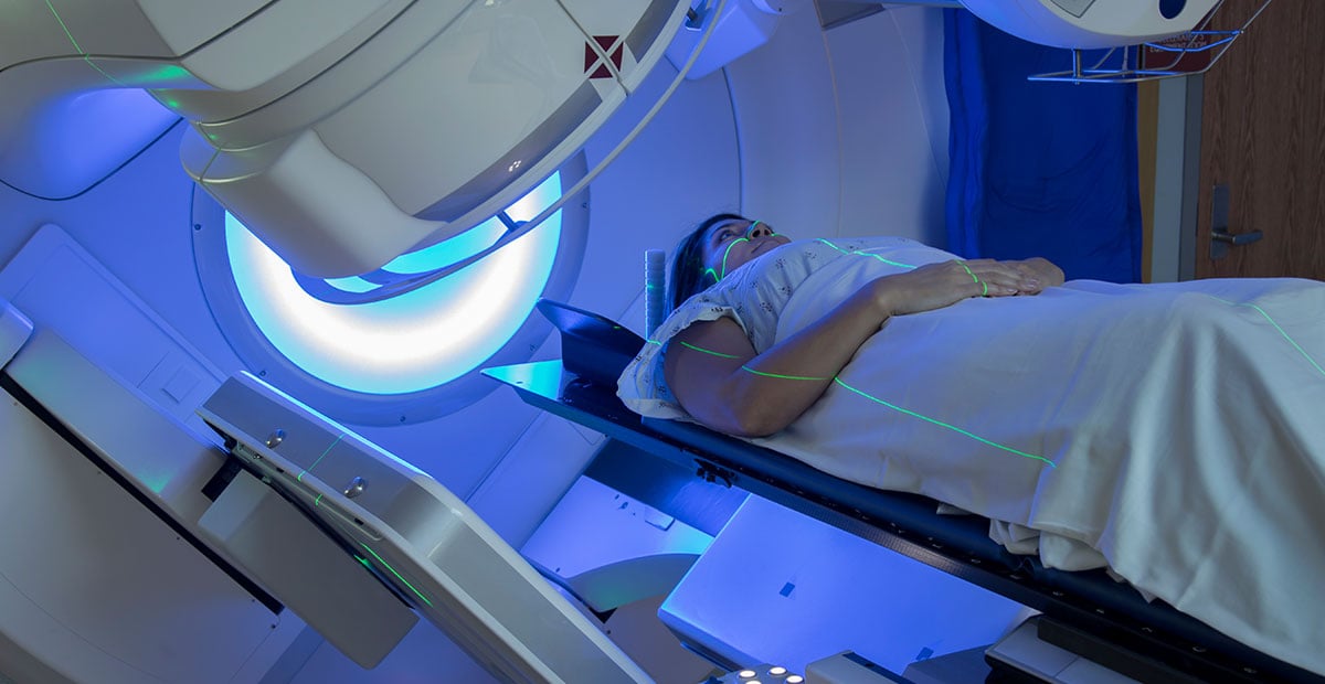 A patient in a gown lies on a table as a radiation therapy machine moves around her