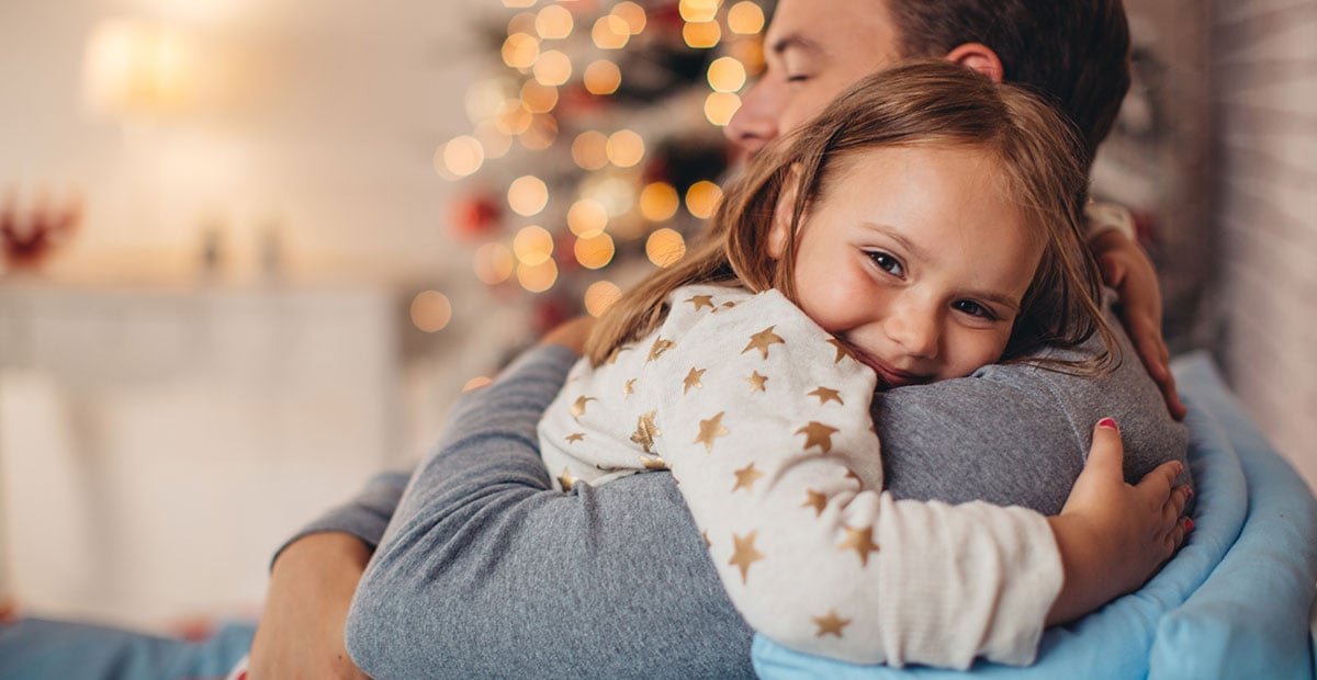 Father and his cute daughter in front of christmas tree, lying on bed. Girl embracing daddy.