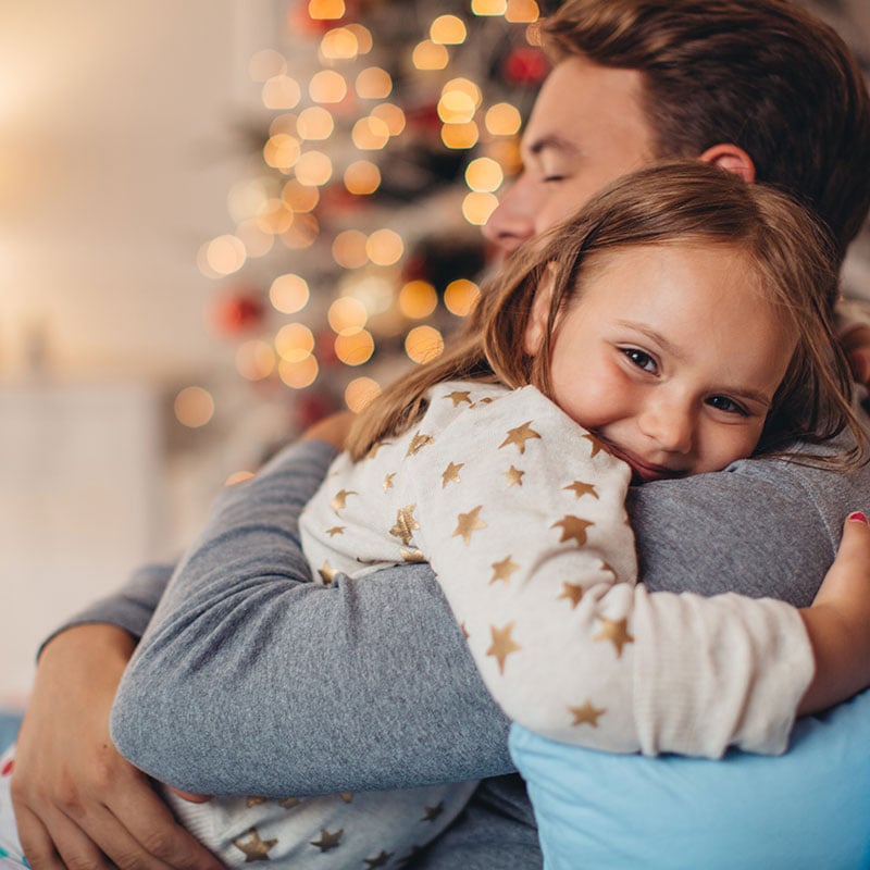Father and his cute daughter in front of christmas tree, lying on bed. Girl embracing daddy.