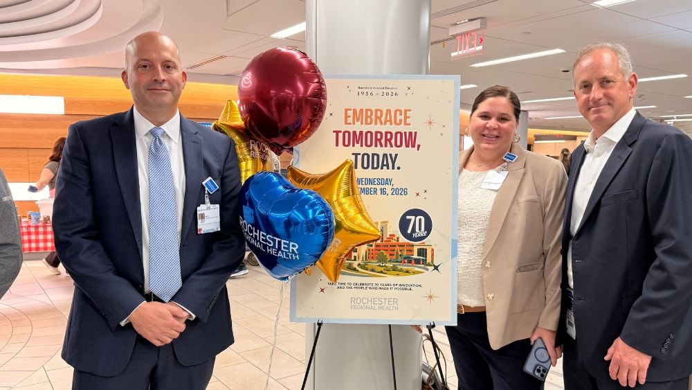 Rochester Regional Health leaders standing next to 70th anniversary poster at Rochester General Hospital