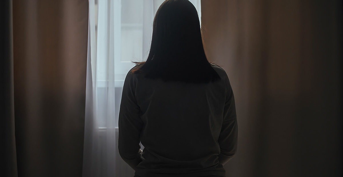 Silhouette of a young woman in pajamas against the background of a window at home on a bed with seasonal affective disorder or depression. The concept of winter depression due to lack of sunlight