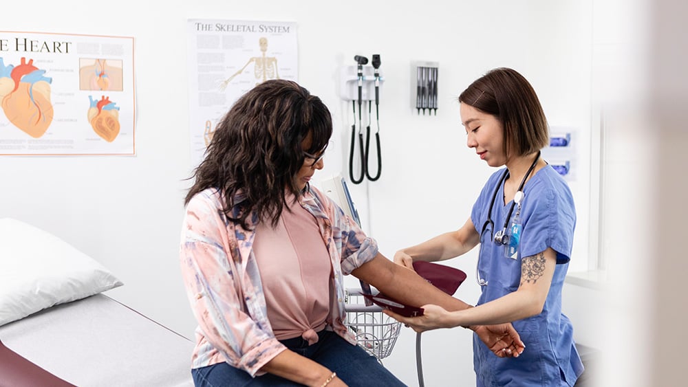 Middle aged female patient having blood pressure taken in medical office by young Asian female doctor