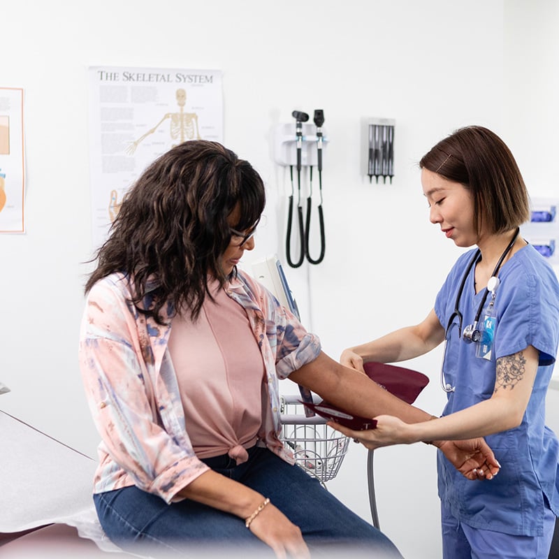 Middle aged female patient having blood pressure taken in medical office by young Asian female doctor