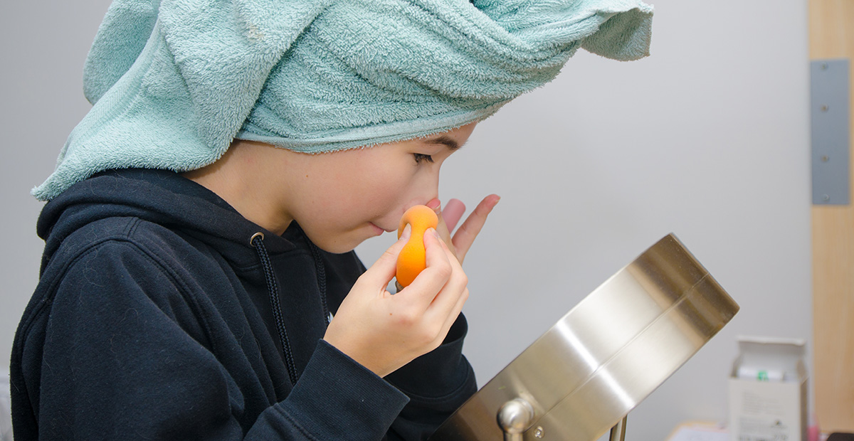 Teenage girl cleaning her face in front of mirror while wearing a towel on head after washing her hair