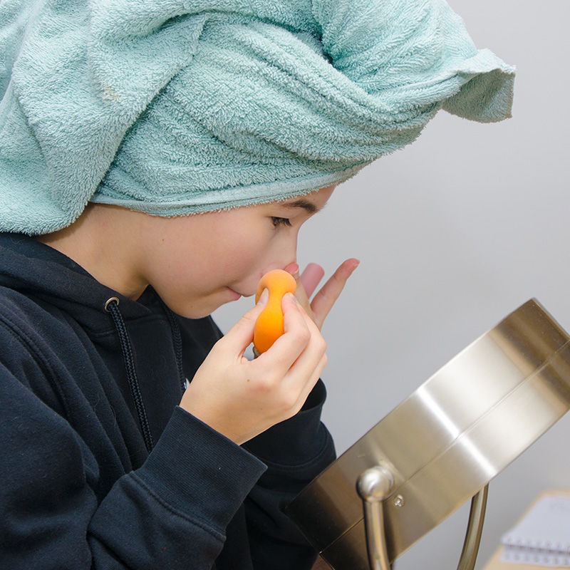 Teenage girl cleaning her face in front of mirror while wearing a towel on head after washing her hair