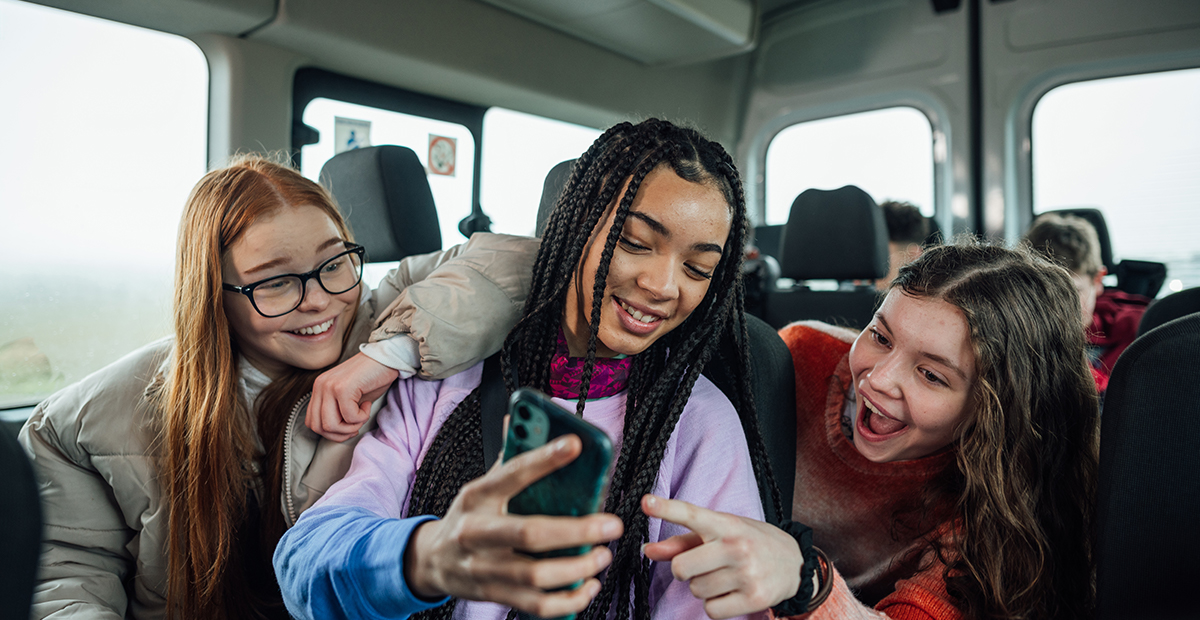 A front view of a group of three teenage girls on the minibus on the way to go on a hiking field trip