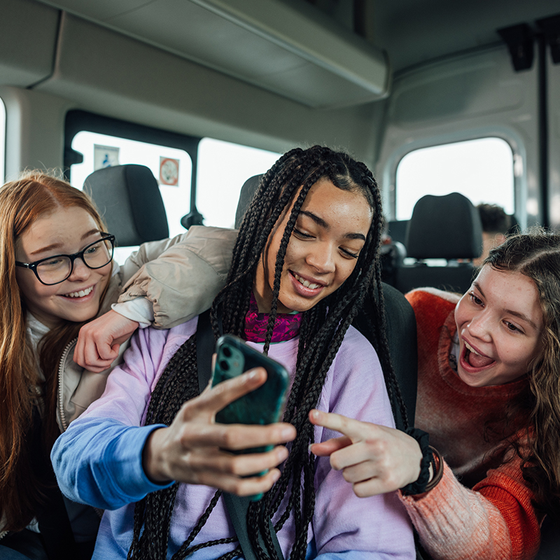 A front view of a group of three teenage girls on the minibus on the way to go on a hiking field trip