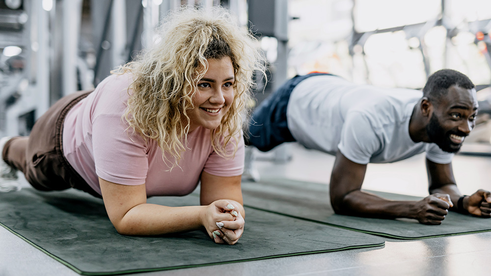 Woman and man doing plank exercise in gym side by side