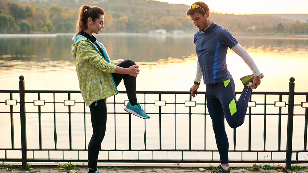 Female runner and male runner stretch outdoors on bridge