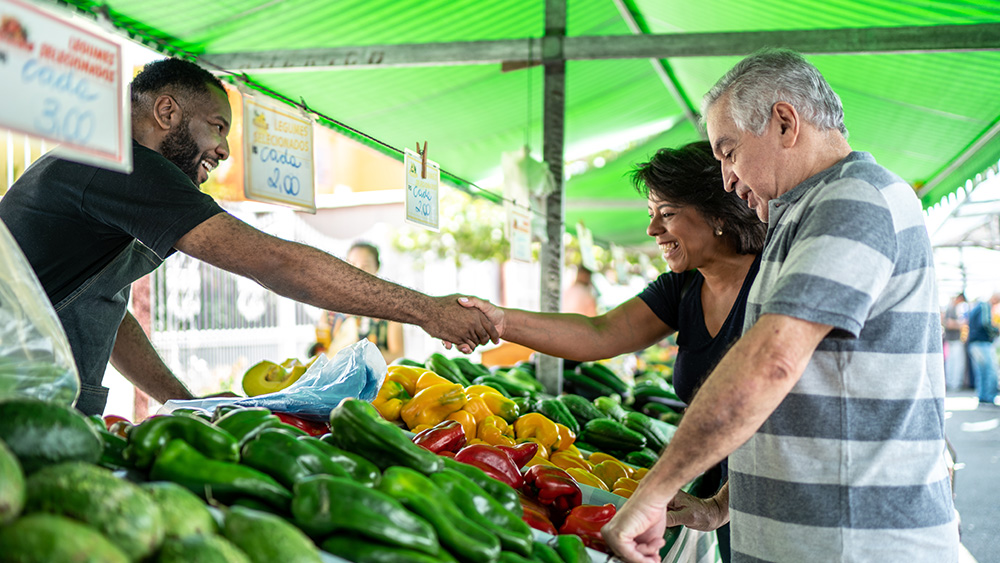 Customer shaking hands with two farmers at outdoor market