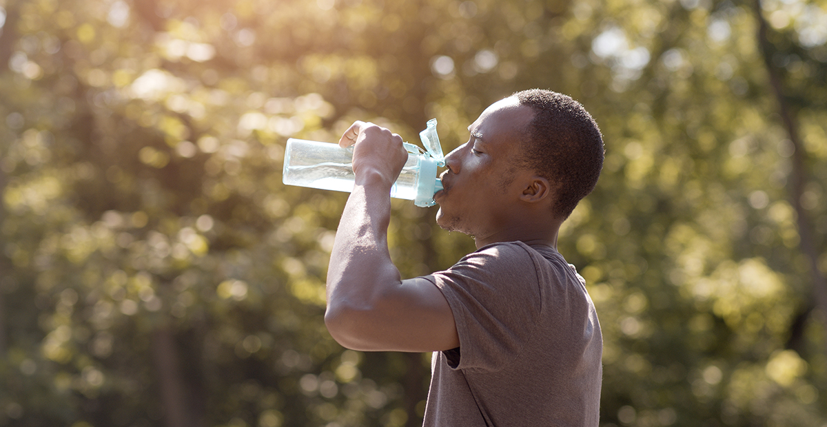 Young Black man drinking water out of clear bottle outdoors