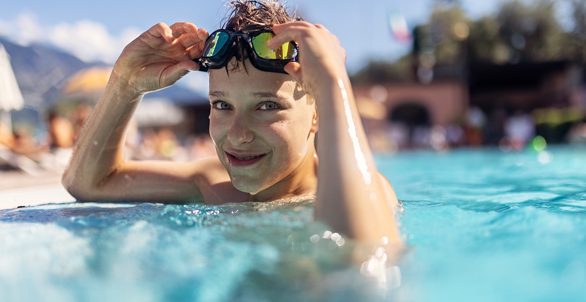 Little boy is practicing in swimming pool. The boy is smiling at the camera