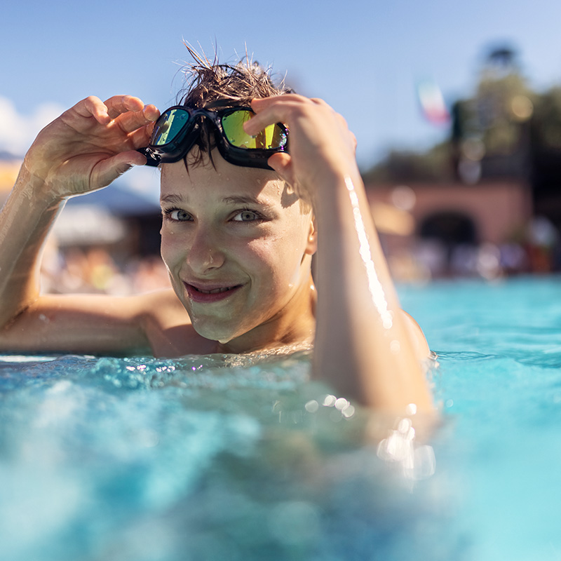 Little boy is practicing in swimming pool. The boy is smiling at the camera
