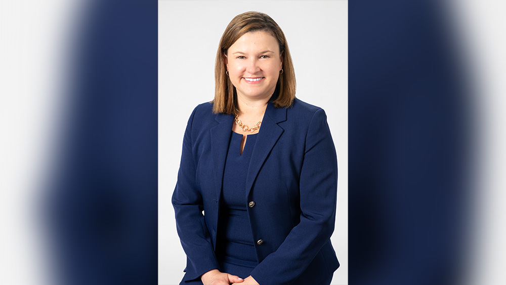 White woman with brown shoulder length hair in blue suit smiles