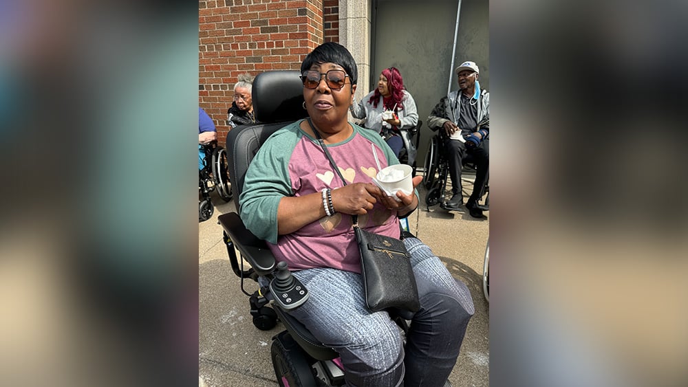 Black woman in motorized scooter wearing sunglasses holds ice cream cup in land