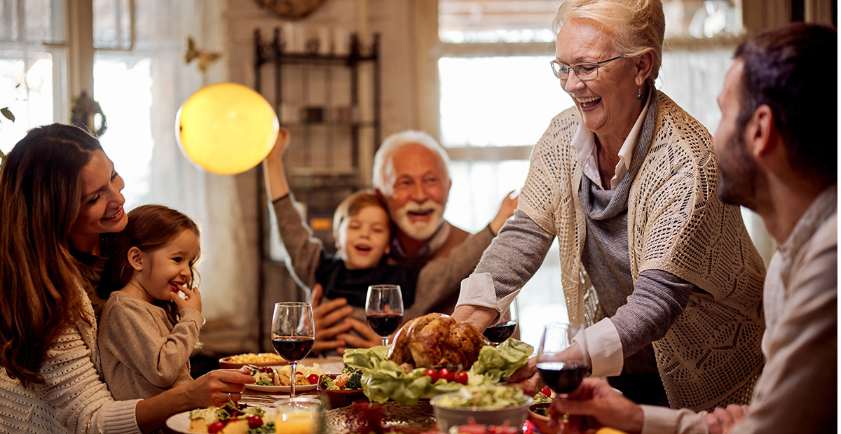 Happy mature woman serving food to her family during Thanksgiving meal at dining table
