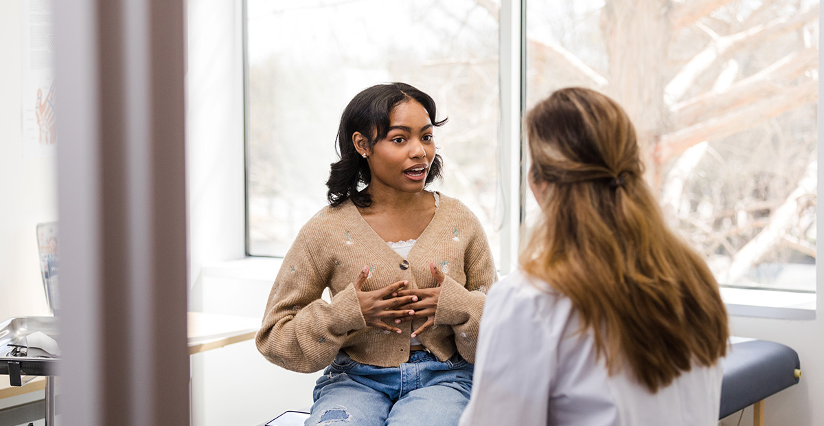 The young adult female patient gestures while explaining her health struggles with the doctor so she can receive some guidance.