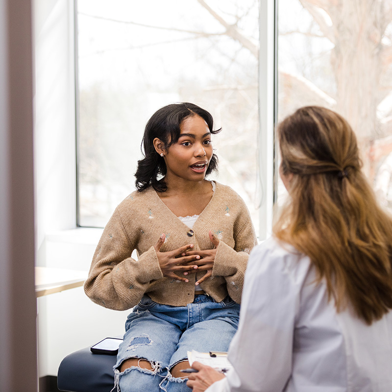 The young adult female patient gestures while explaining her health struggles with the doctor so she can receive some guidance.
