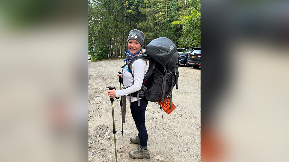 White woman carrying hiking pack walking poles standing at trailhead