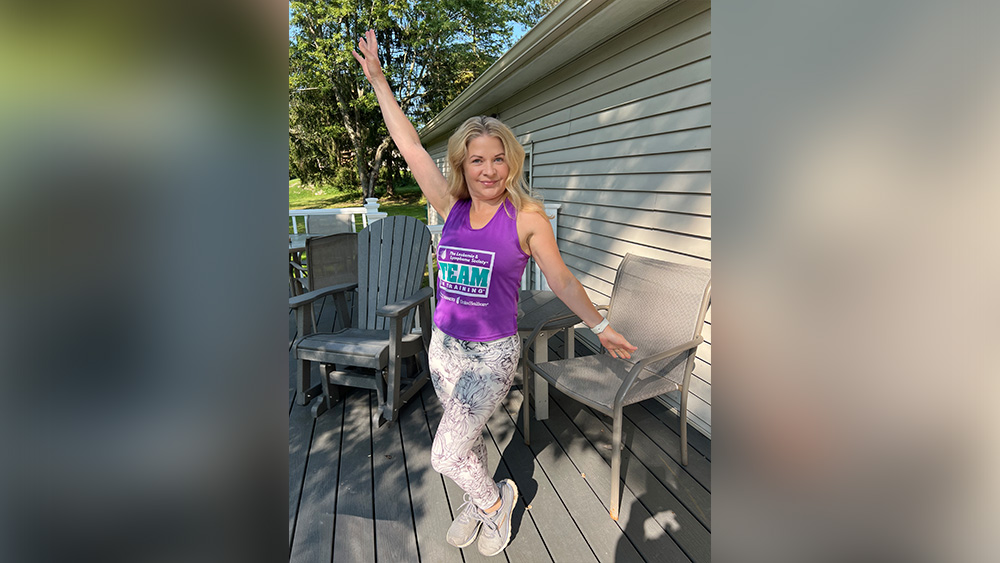 White woman blonde hair in purple shirt and white leggings posing for camera on deck