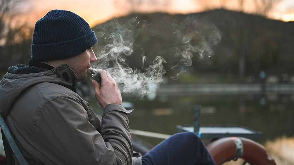 Young man vaping outdoors in cold weather