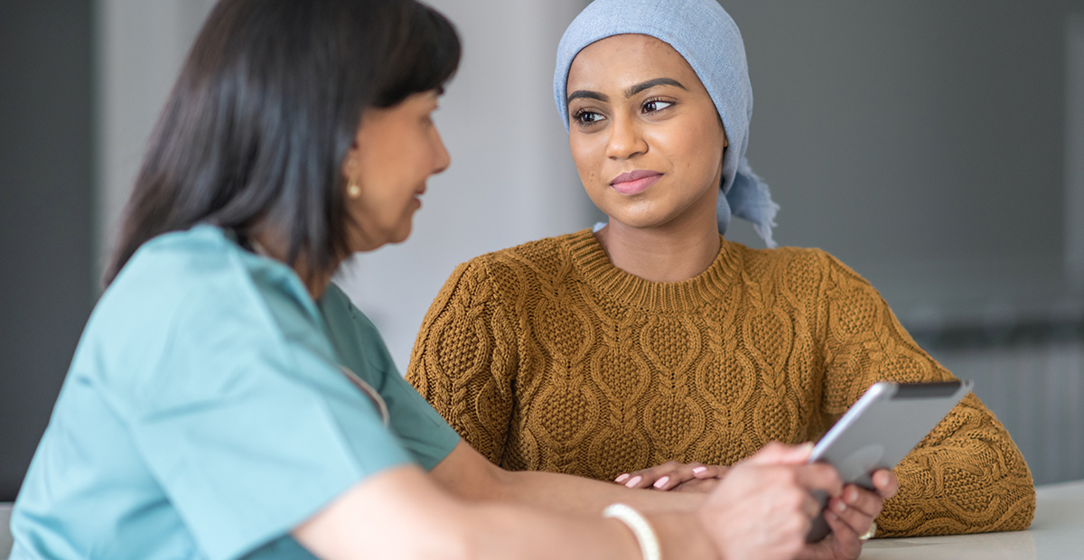 Young woman wearing head wrap talks with female doctor at table