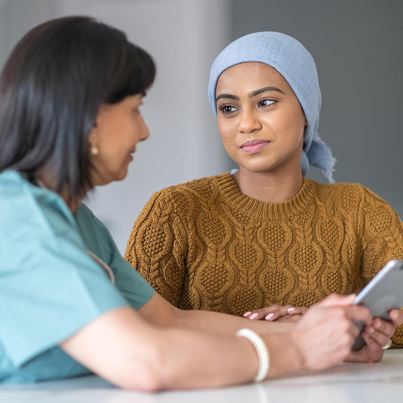 Young woman wearing head wrap talks with female doctor at table