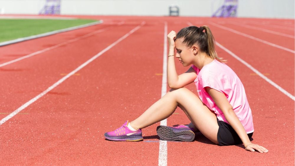 Young female track athlete sitting down on track