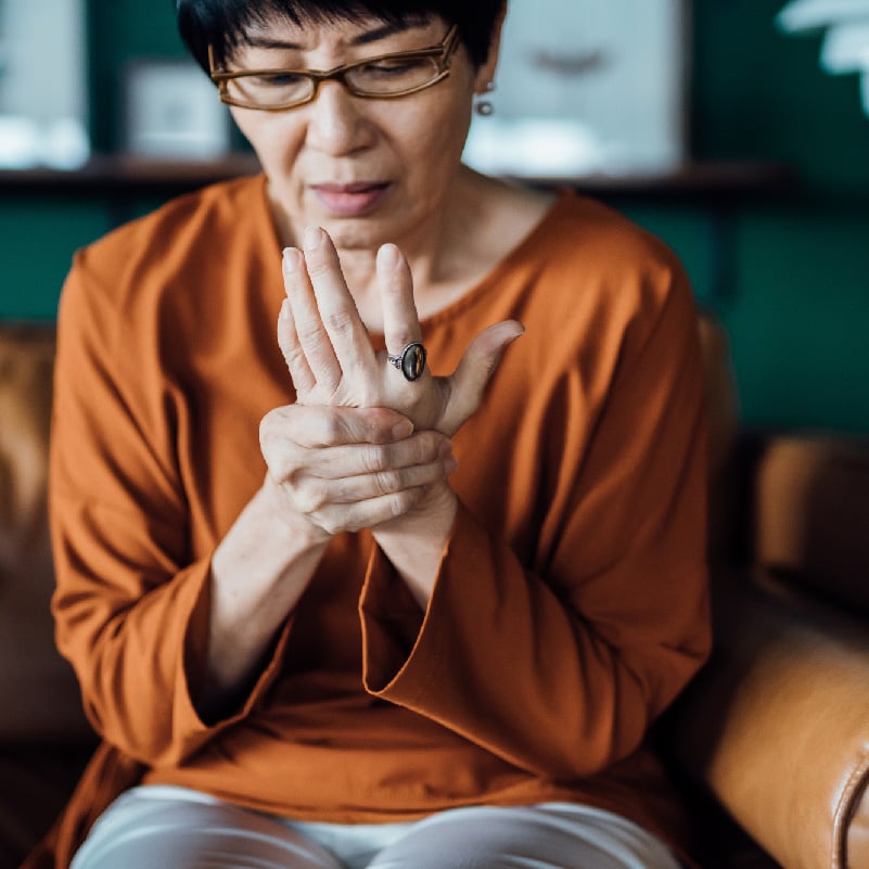 elderly female sitting down holding her hand in pain