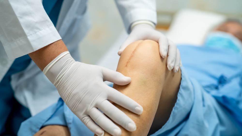 A provider looks closely at a knee replacement surgical patient