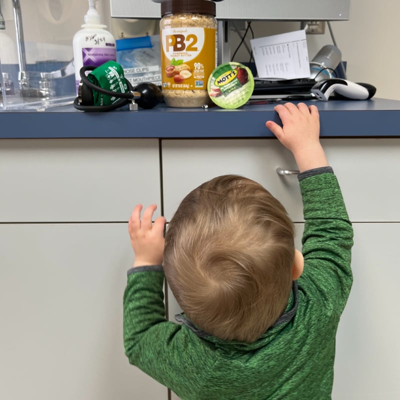 Jackson, a toddler, reaches up toward a countertop in a pediatric office