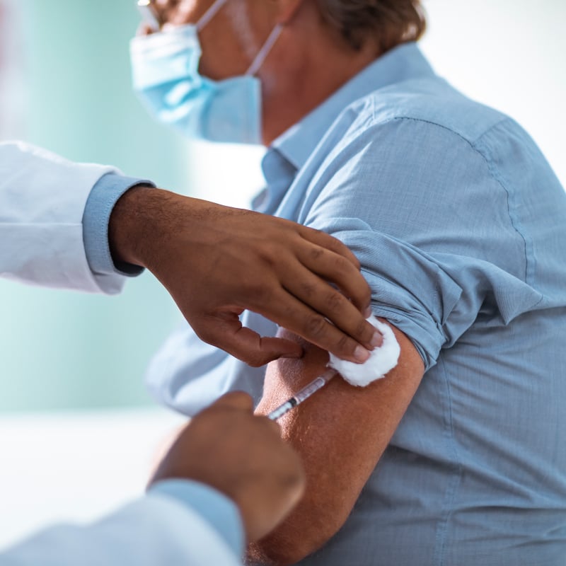 A patient wearing a mask is given an injection by a medical provider