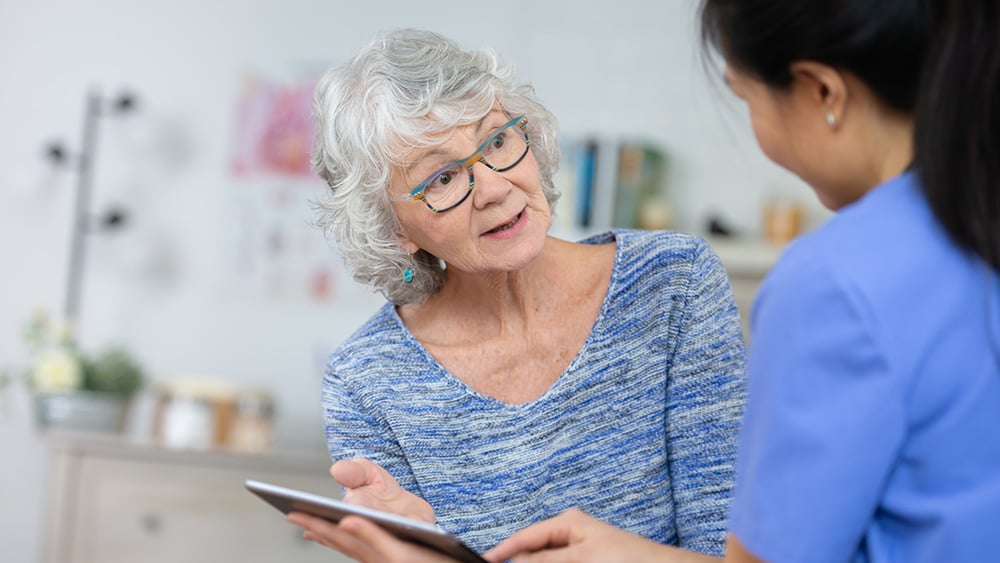 A senior woman speaks to her doctor about her health. She looks at her doctor after she explained to her what she needs to be healthy. The doctor is holding a tablet.