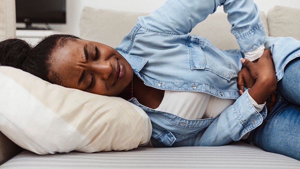 Woman in painful expression holding hands against belly