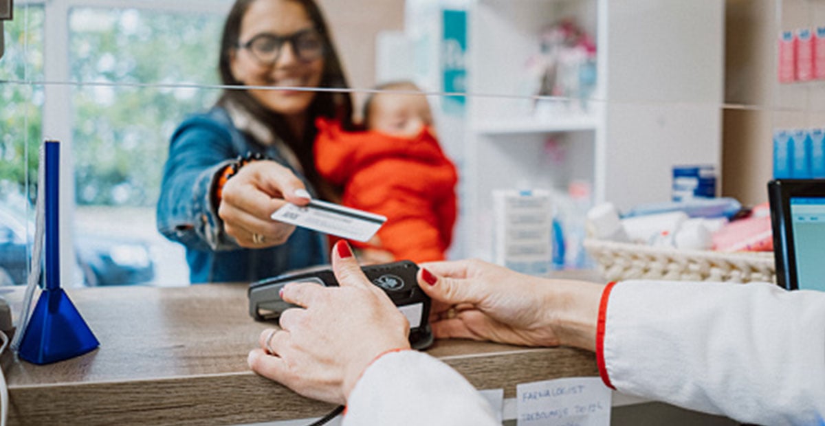 Smiling mother holding child hands credit card to receptionist at doctor's office