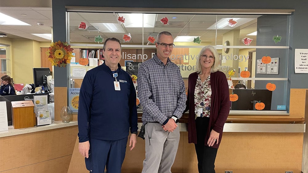 White patient smiles while taking a photo with two providers - one man and one woman