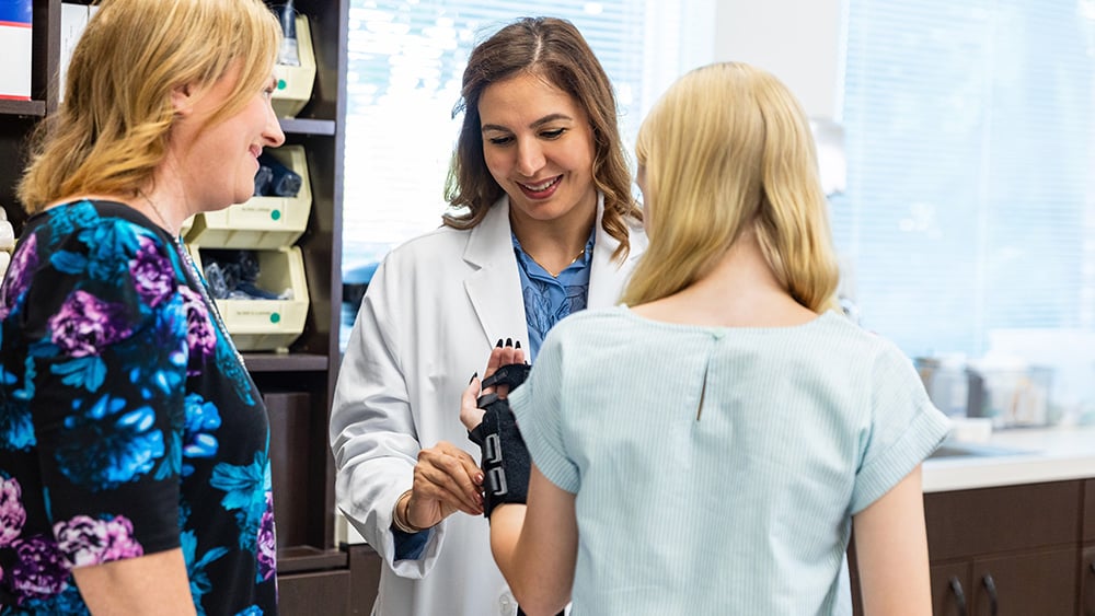 Female doctor helps young woman put on wrist brace.