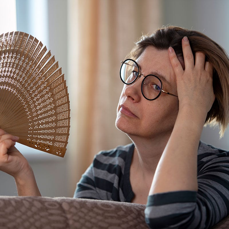 Exhausted middle aged woman waving her fan, suffering from menopausal symptoms, experiencing hot flush