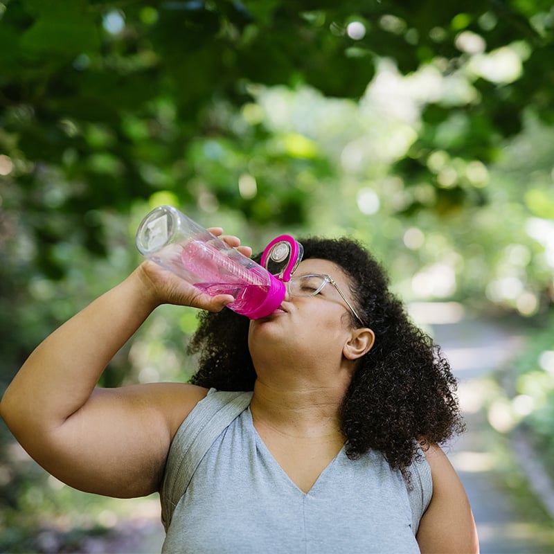 Black woman with natural hair on nature trail drinking out of pink water bottle
